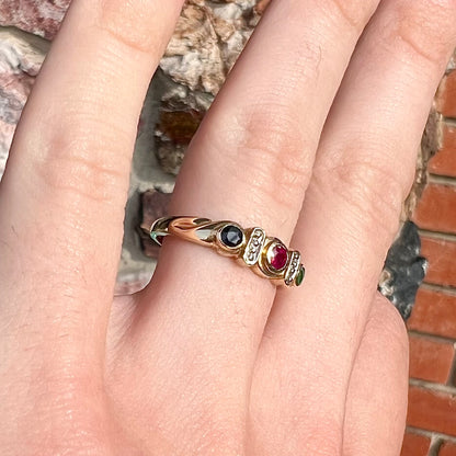 Three stone ring set with blue sapphire, lab created ruby, emerald, and two small diamonds in yellow gold.