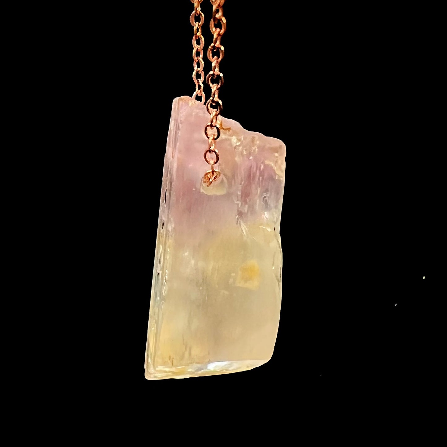 A drilled bicolor spodumene crystal hanging on a copper cable chain.  The crystal is pink and yellow, or kunzite and triphane respectively.