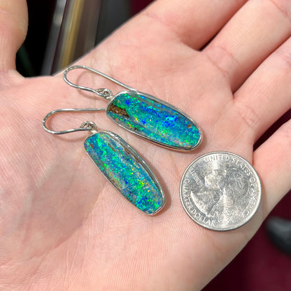 A pair of white gold boulder opal French wire dangle earrings.  The opal is predominantly glimmery blue.