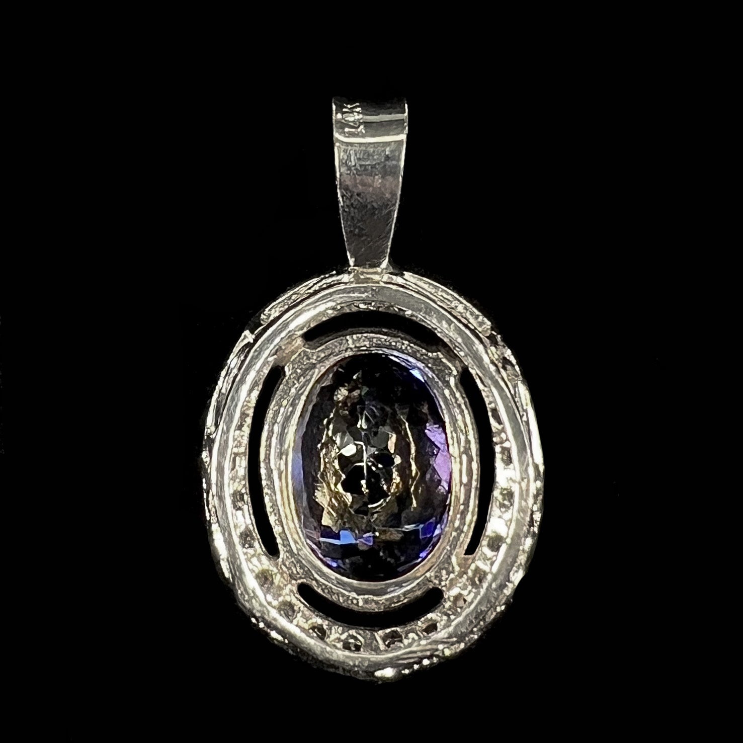 A ladies' 14kt white gold tanzanite and diamond halo pendant.  The sides of the pendant have filigree.