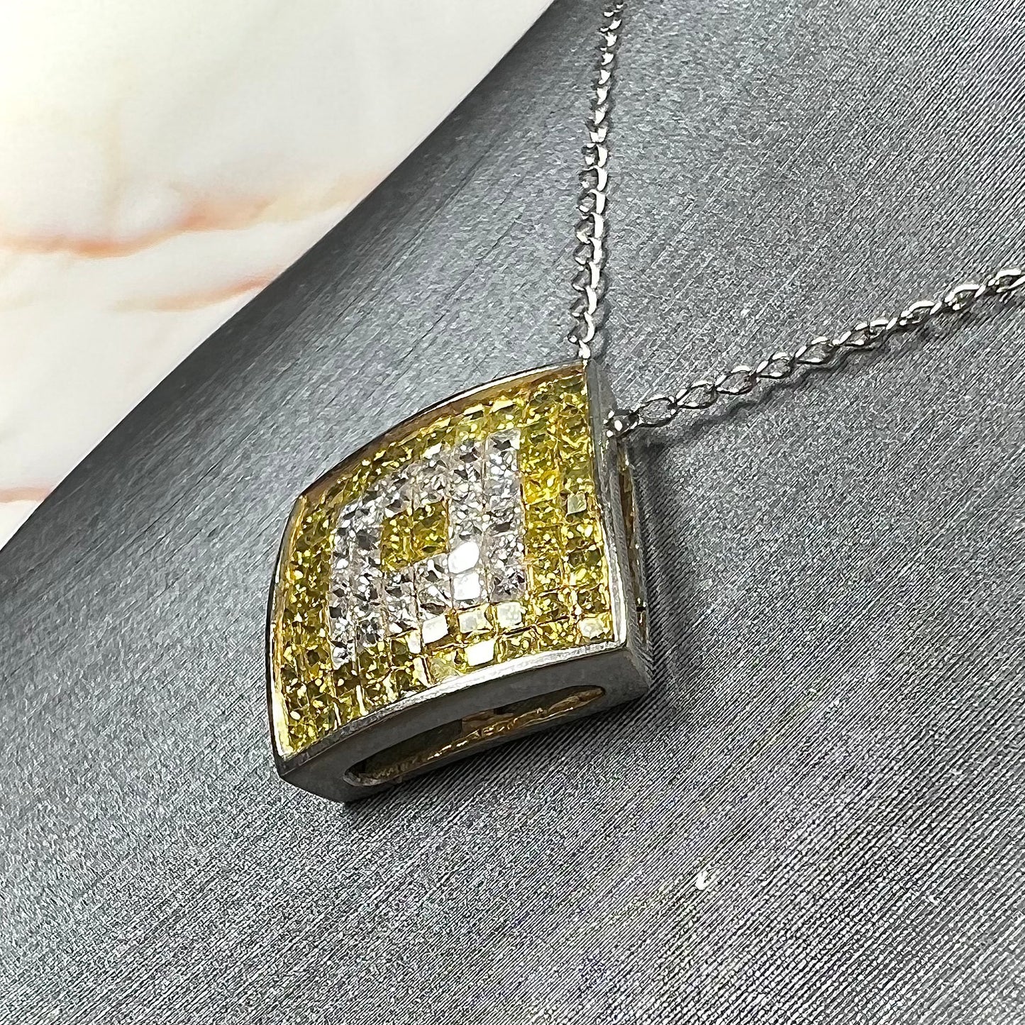 A square shaped necklace set with princess cut yellow and white diamonds in a white gold setting on a white gold chain.