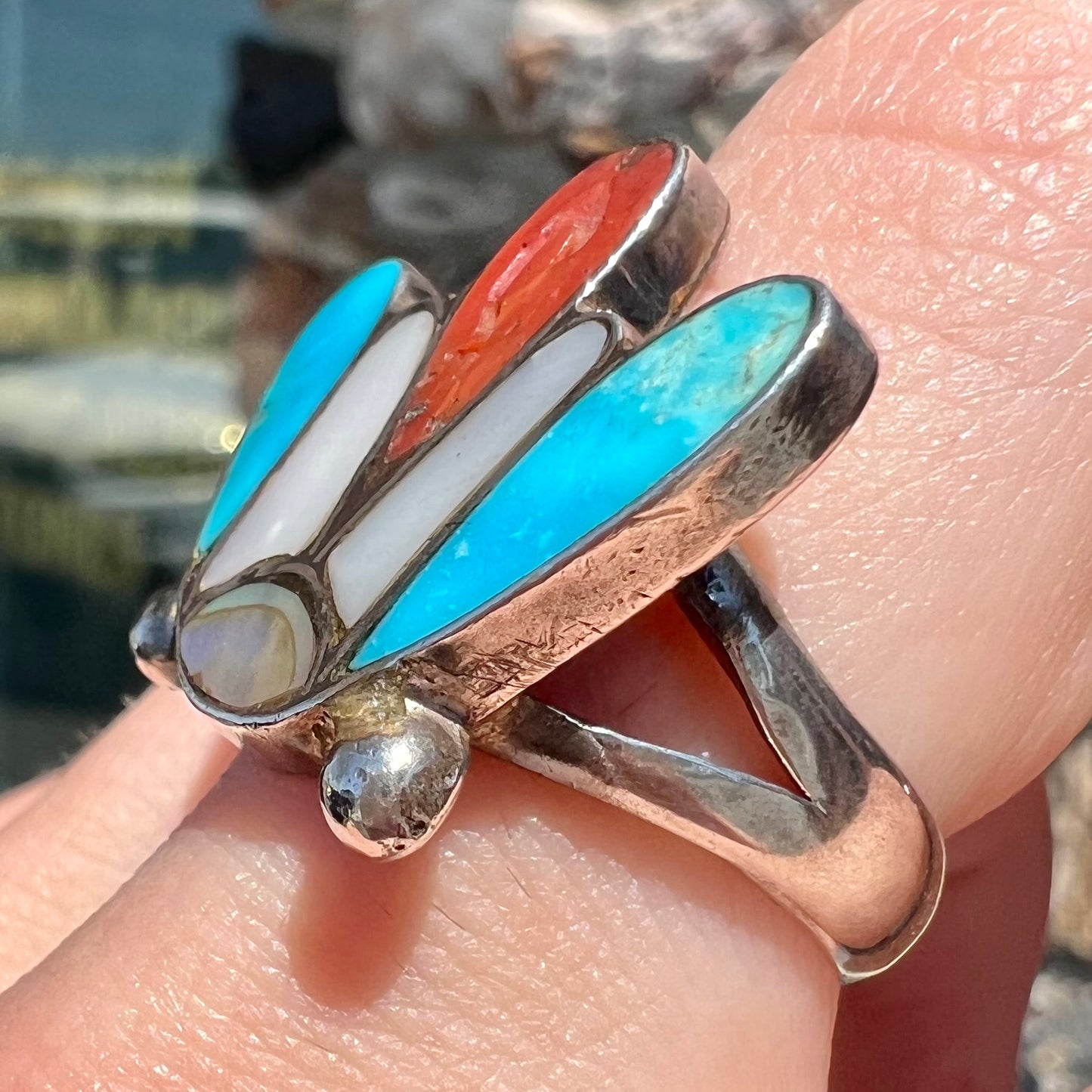 A turquoise, coral, and mother of pearl stone inlay ring made in the motif of a Zuni Indian headdress.