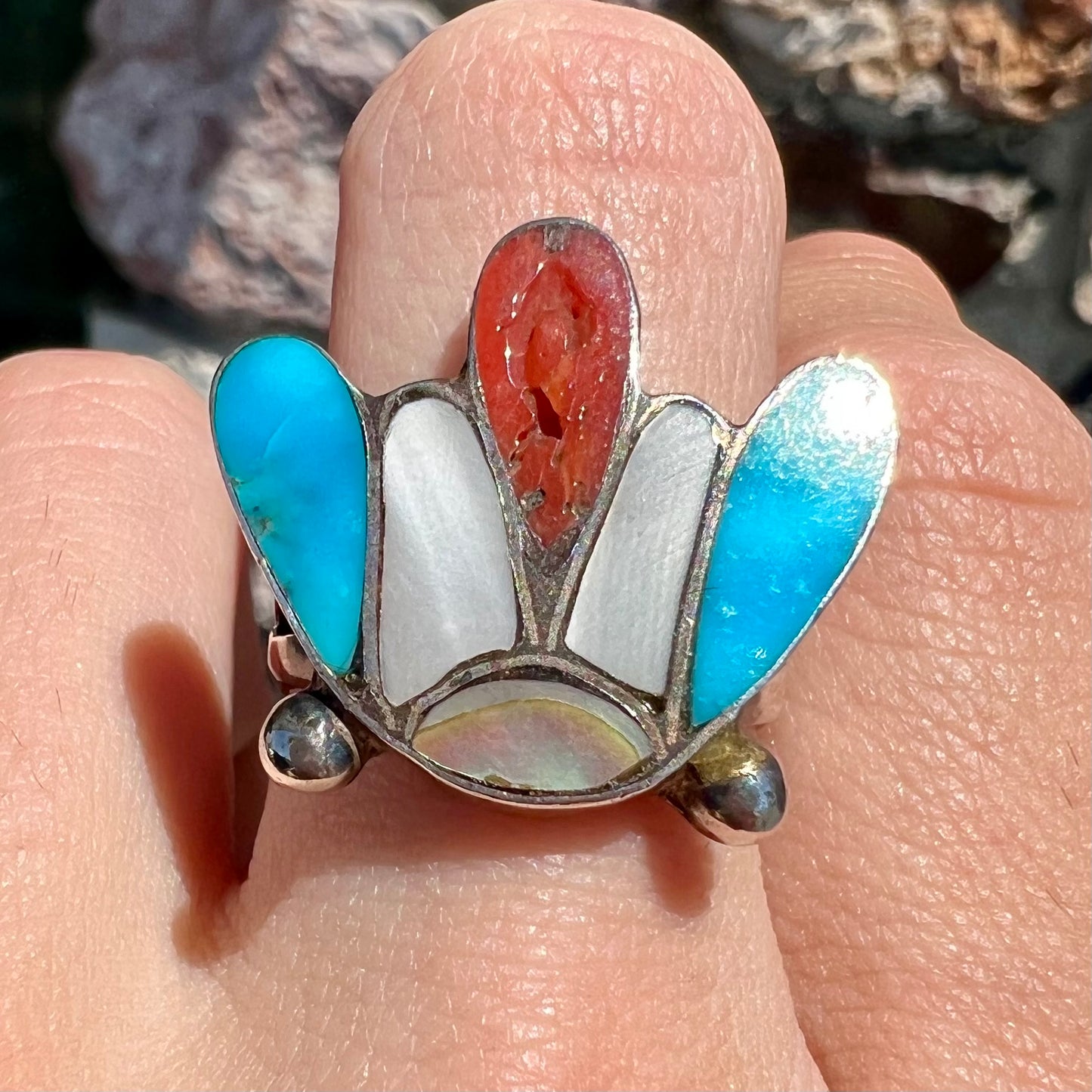 A turquoise, coral, and mother of pearl stone inlay ring made in the motif of a Zuni Indian headdress.