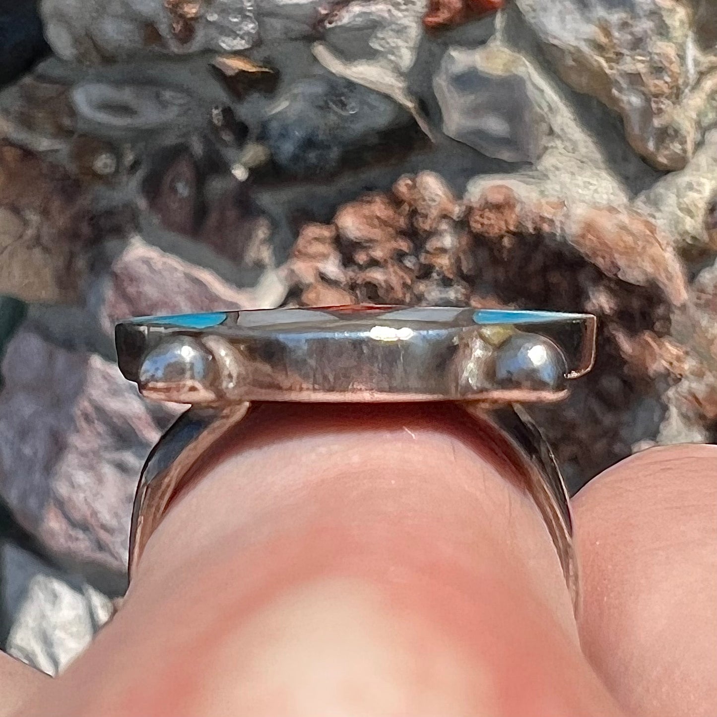 A turquoise, coral, and mother of pearl stone inlay ring made in the motif of a Zuni Indian headdress.